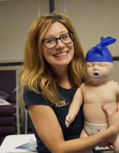Photo of Kelli holding training manikin with a disposable glove on it's head.